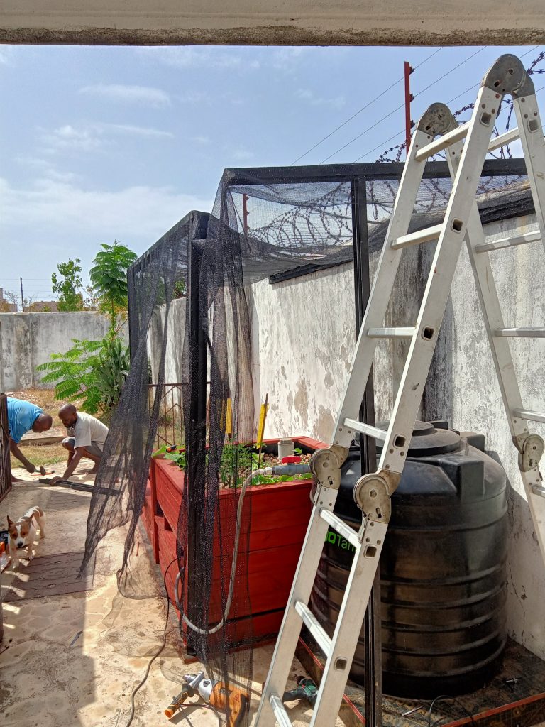 A team building an aquaponic system under a shade structure, demonstrating sustainable farming practices and water-efficient agriculture in a rural Kenyan setting.