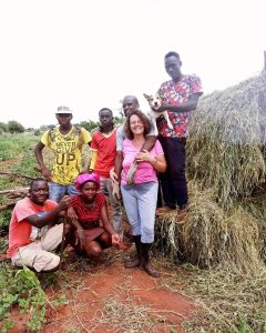 Group of local community members and a woman standing together in front of stacked hay, showcasing collaborative efforts in sustainable farming practices.