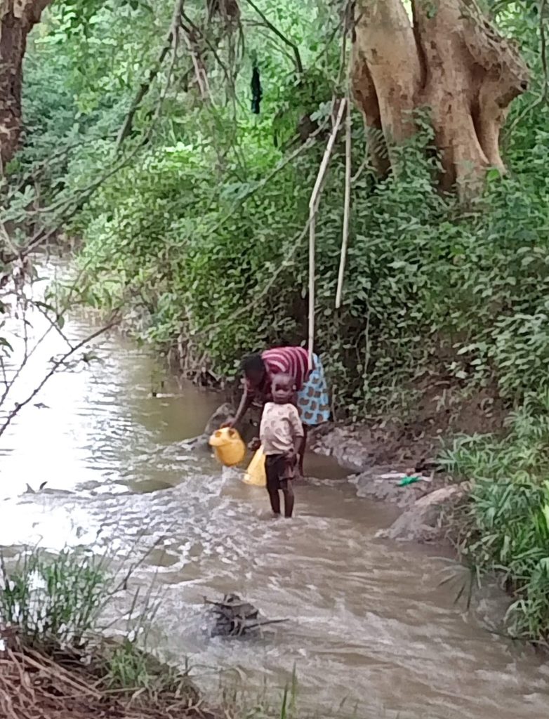 Women fetching river water with jerry cans in a rural area, highlighting the community's reliance on unsafe water sources due to limited access to clean water."