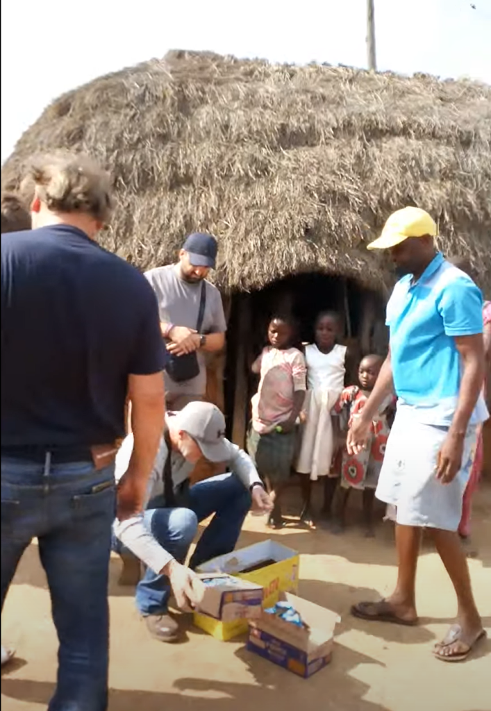 Visitors distributing supplies to families in front of a traditional hut, showcasing community support efforts in rural Kenya.